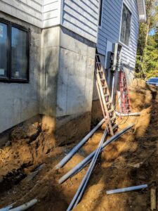 Underground electrical conduit installation in a trench next to a house foundation by E & E Electric in Post Falls, ID.