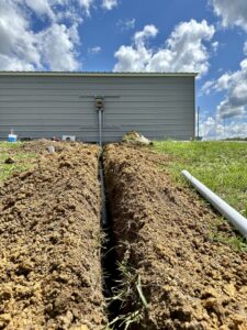 Underground electrical conduit installation in a trench leading to a building by Lighten Up Electric, LLC in Cranston, RI.