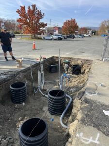 An excavated trench showing underground electrical conduits and utility pipes being installed by Peeler Electric Light & Power in Merrimack, NH.
