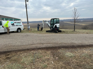 Pro Circuit Electric van and crew performing underground electrical installation with an excavator near a utility pole in Peoria, IL.
