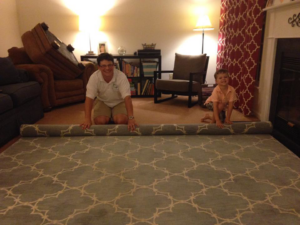 A man and child unrolling a large area rug during an installation service by All Clean of the Triad in High Point, NC.