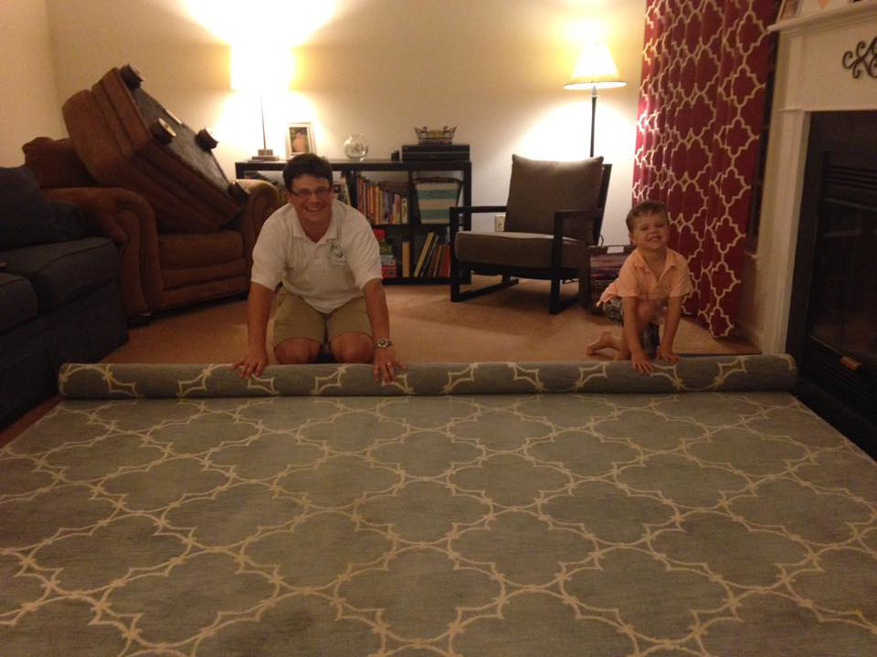 A man and child unrolling a large area rug during an installation service by All Clean of the Triad in High Point, NC.