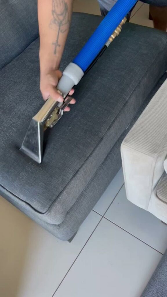 A professional cleaning a grey sofa cushion with an upholstery cleaning tool, performed by Good Guys Carpet Cleaning in Katy, TX.