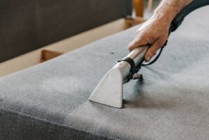 A professional cleaning a sofa cushion with an upholstery tool by North Seattle Carpet Cleaning in Seattle, WA