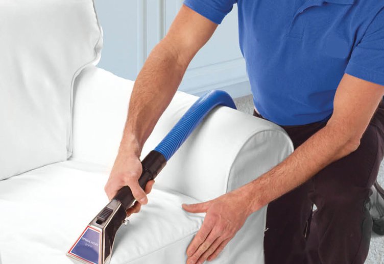 A professional cleaning a white sofa with an upholstery cleaning tool, a service offered by Alpine Carpet Care in Medford, OR.