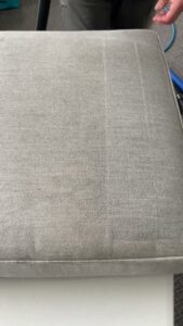 A professional cleaning a sofa cushion, showing a clean strip, by Atlanta Top Force Carpet Cleaning in Roswell, GA.