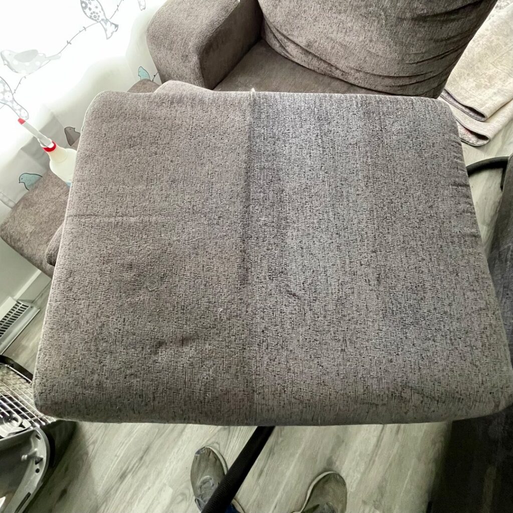 An upholstery cushion being cleaned, showing a clear before and after section, by Columbia Carpet Cleaning in Columbia, MO.