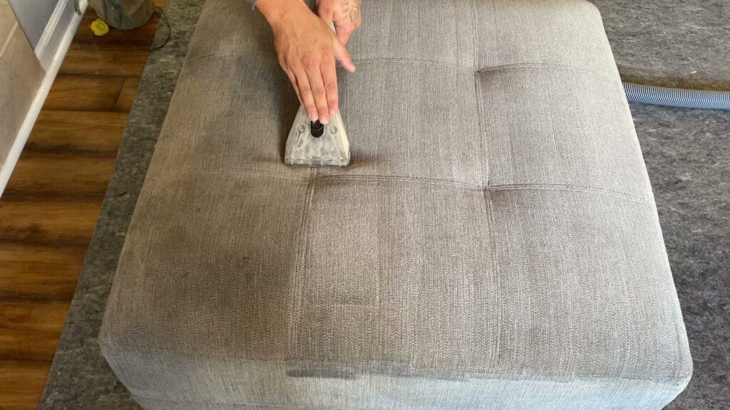 A professional cleaning an upholstered ottoman with a specialized tool at Believe That Carpets & Upholstery Cleaning in Colorado Springs, CO.