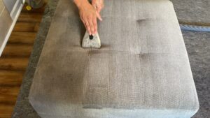 A professional cleaning an upholstered ottoman with a specialized tool at Believe That Carpets & Upholstery Cleaning in Colorado Springs, CO.