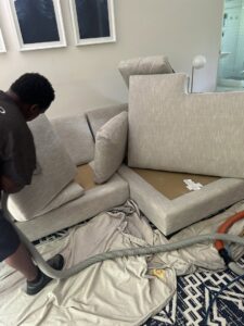 A professional cleaning an upholstered sectional sofa by Treo General Services of North Carolina LLC in Durham, NC.