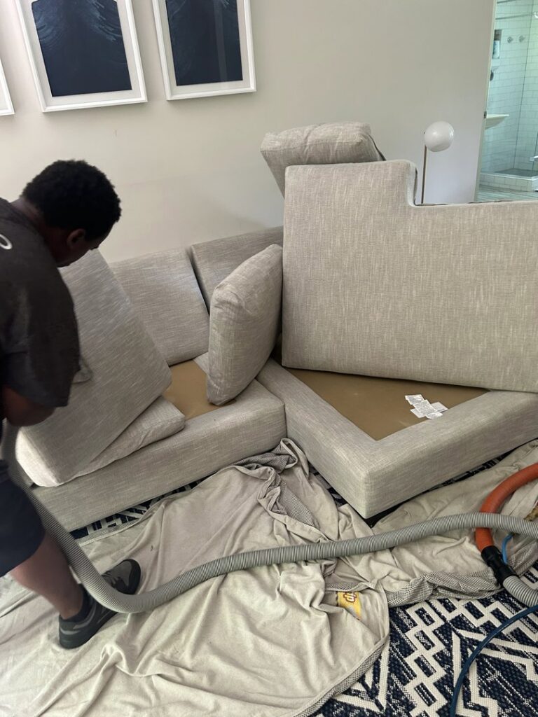 A professional cleaning an upholstered sectional sofa by Treo General Services of North Carolina LLC in Durham, NC.