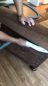 A professional cleaning a brown upholstered sofa with a specialized tool at Alex's Janitorial and Carpet Cleaning in Bakersfield, CA