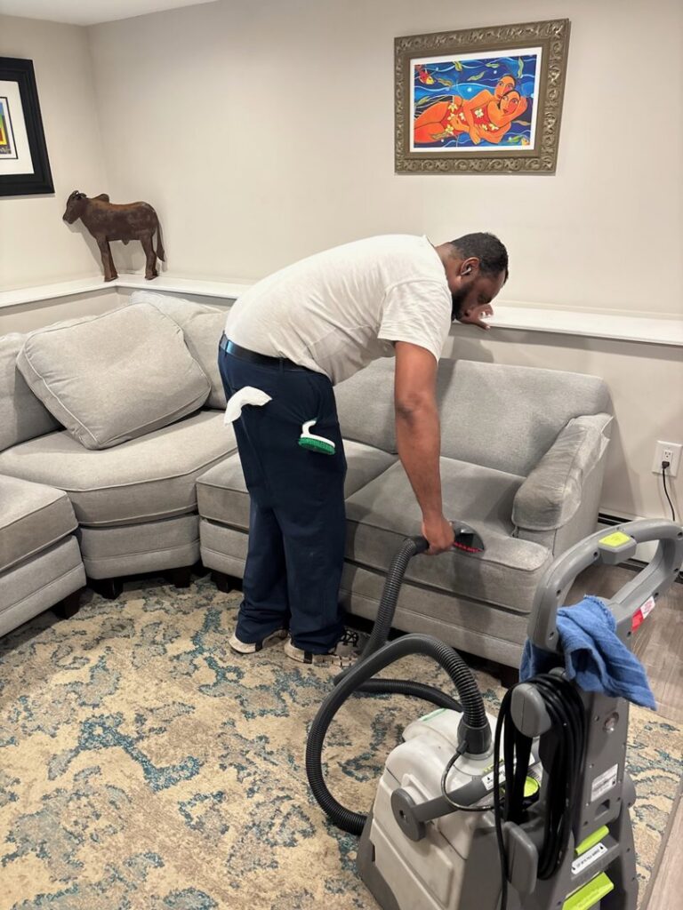 A professional cleaning a grey sectional sofa with an upholstery tool by Ready2go Professional Carpet & Upholstery Cleaning in Boston, MA