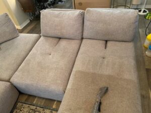 An upholstery cleaning tool cleaning a light-colored sofa sectional by D&H Anytime Carpet Cleaning LLC in Mobile, AL.