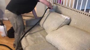 A professional performing upholstery cleaning on a sofa with a specialized tool for Ecodry Carpet Cleaning Las Vegas, NV.