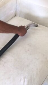 A professional cleaning a white upholstered sofa with a specialized tool at Alex's Janitorial and Carpet Cleaning in Bakersfield, CA
