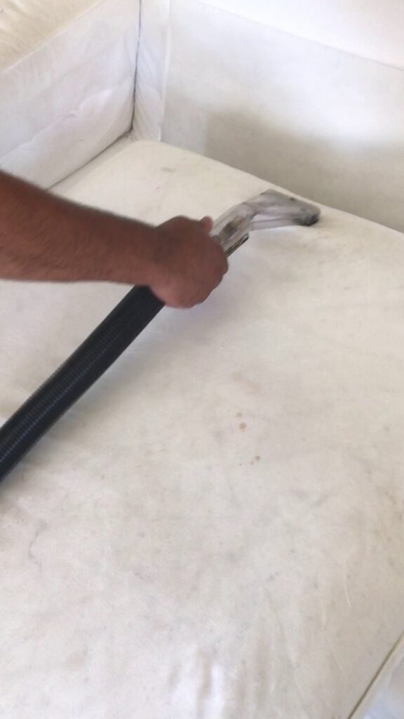 A professional cleaning a white upholstered sofa with a specialized tool at Alex's Janitorial and Carpet Cleaning in Bakersfield, CA