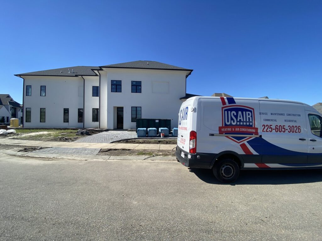 A US AIR service van parked in front of a large new residential building, indicating HVAC installation in Baton Rouge, LA.
