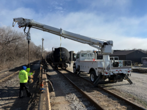 A utility truck with an auger attachment on railroad tracks, likely for electrical pole installation or repair by Pro Circuit Electric in Peoria, IL.