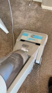 A vacuum cleaner on a carpet, showing collected dirt, part of the carpet cleaning process by Soft N Dry in Tucson, AZ.