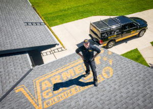 A Varment Guard technician standing on a residential roof with a company truck visible, indicating wildlife control services in Danville, IN.
