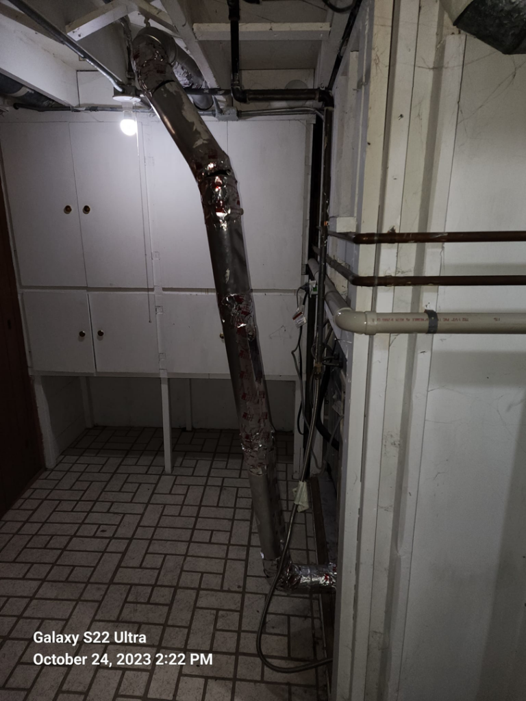 A large vertical dryer vent duct in a utility room with a tiled floor, serviced by Pro Power Air Duct & Dryer Vent Cleaning in Kenosha, WI.