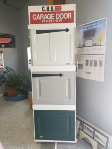 A vertical display stand showcasing white, grey, and green garage door panel samples at B's Quality Door, Inc. in Enid, OK.