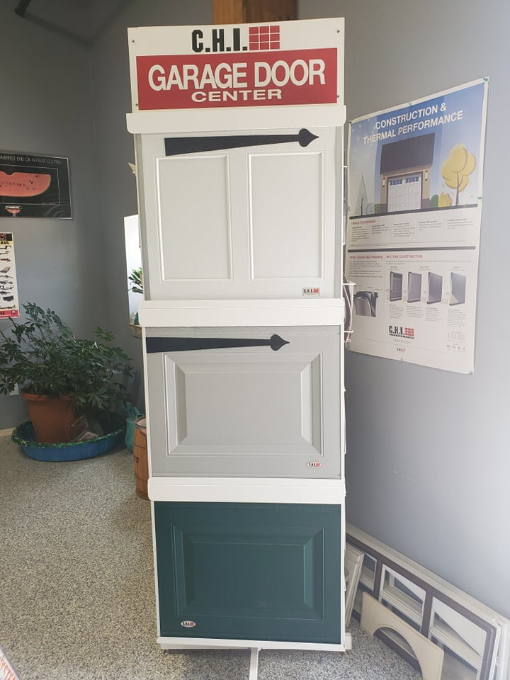 A vertical display stand showcasing white, grey, and green garage door panel samples at B's Quality Door, Inc. in Enid, OK.