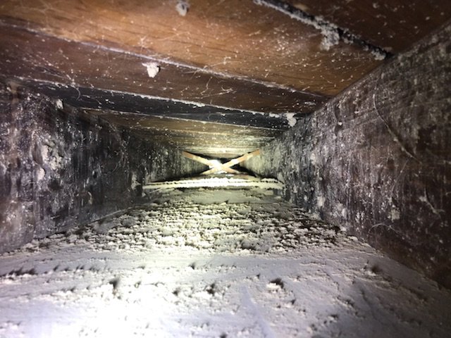 A view inside a very dirty wooden air duct with heavy dust and cobwebs, requiring cleaning by Vacman Air Duct Cleaning in South Bend, IN