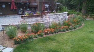A vibrant flower bed with a stone wall, bordering a neatly maintained lawn, reflecting the quality of Nice Grass Minnesota LLC in Minneapolis, MN.