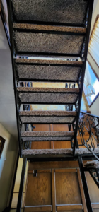 An upward view of a newly carpeted staircase with dark brown treads and wrought iron railings by B A Carpet and Flooring in Broken Arrow, OK.