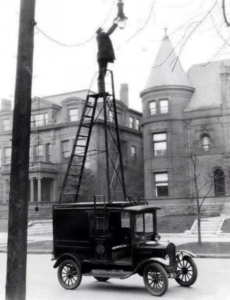 A vintage electrician repairing a street light from a utility truck, representing the long history of electrical work by Norway & Sons, Inc. in Barre, VT.