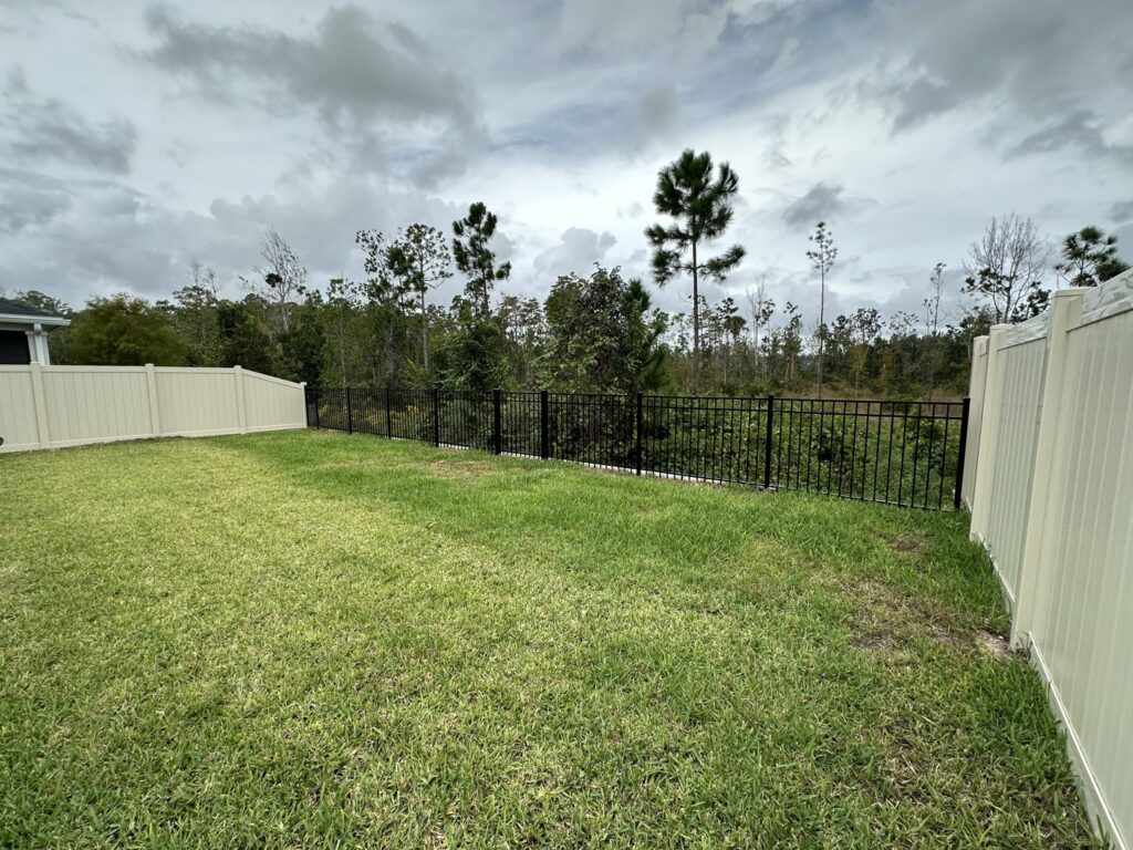 A backyard featuring a combination of tan vinyl and black aluminum fencing by Masters Fence Contracting in Jacksonville, FL.
