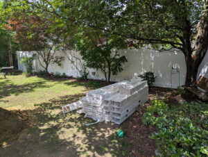 A stack of white vinyl fence panels and posts ready for installation in a backyard by Brodeur-Campbell Fence Co. in Springfield, MA.