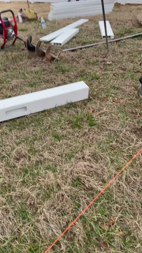 White vinyl fence materials and tools on the ground at a job site by Fenceitforu LLC in Matthews, NC.