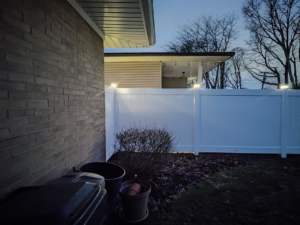 White vinyl fence with post lights installed alongside a brick house by Fence Guys INC in Cleveland, OH.