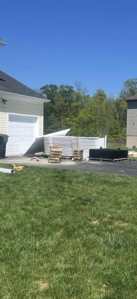 Stacks of white vinyl and black metal fence materials on a driveway for Fence Pros LLC in Medford, OR.