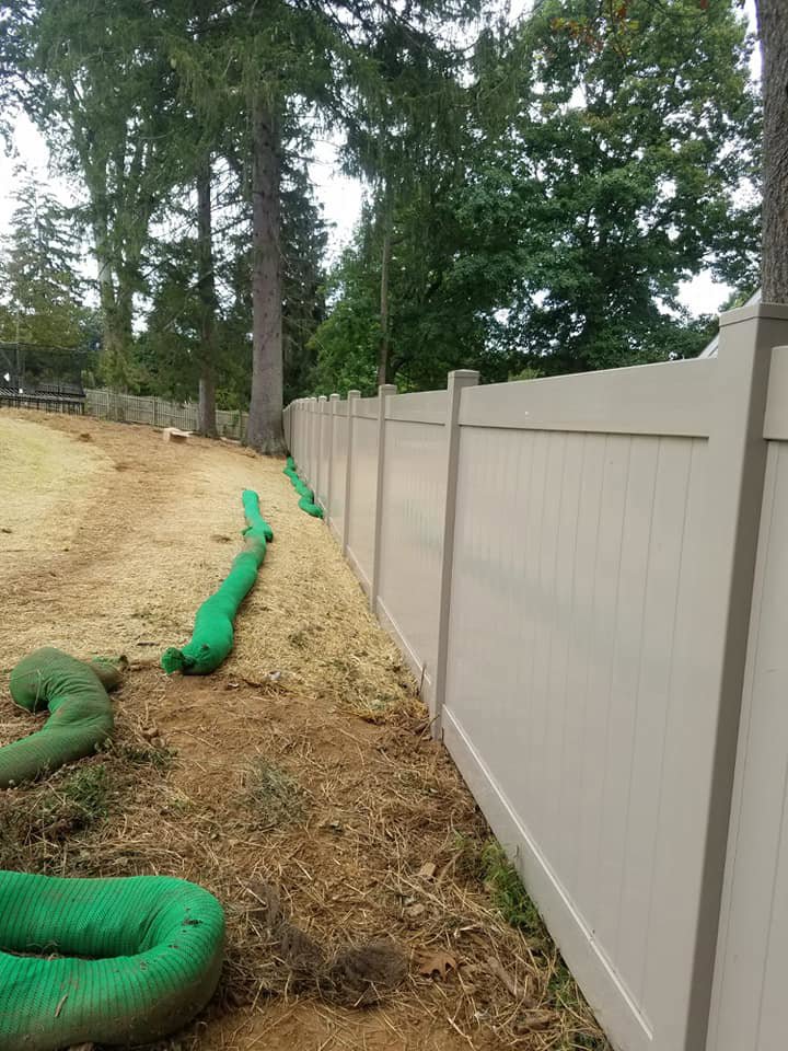 A newly installed light-colored vinyl privacy fence with green erosion control socks by Concord Fence Llc in Wilmington, DE