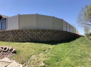 A durable vinyl privacy fence expertly installed on a stone retaining wall by Discount Fence Supply in Great Falls, SC.