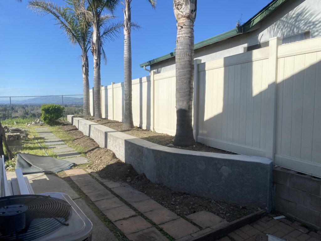 A light-colored vinyl privacy fence installed on a sloped backyard with palm trees by Superior Fence & Rail in San Jose, CA.