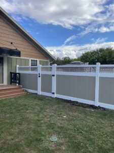 A vinyl privacy fence with a lattice top and gate, installed next to a house by NBBJ Fence LLC in Bluffton, IN.