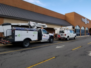 Two Visual Electric, Inc. service vehicles, including a bucket truck for LED lighting, parked outside a Food Lion in Frederick, MD.