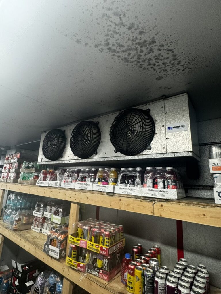 An interior view of a walk-in cooler showing a large refrigeration unit above shelves by Setpoint Refrigeration LLC in Liberty Hill, TX