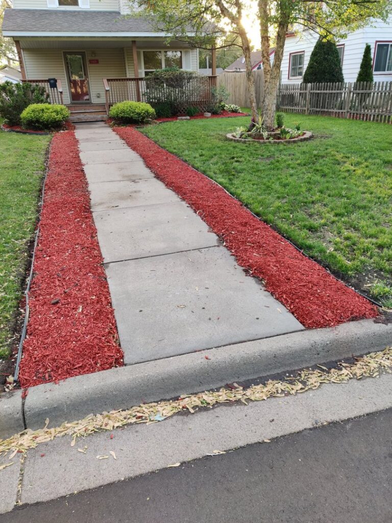 A residential walkway bordered by fresh red mulch and plants, showcasing K&R Lawn Care's landscaping services in Pass Christian, MS.