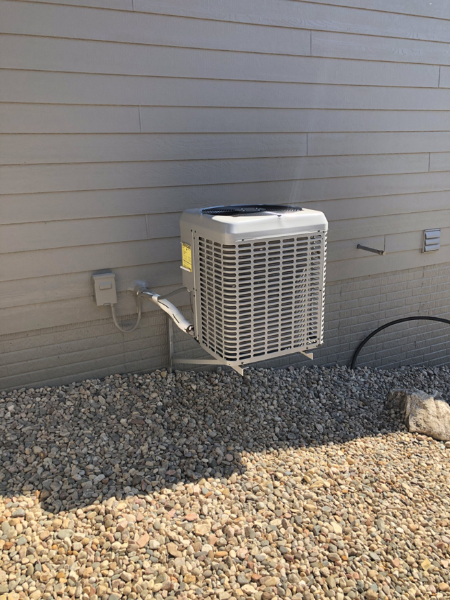 A wall-mounted outdoor AC unit installed on a bracket next to a house by Air Care, an HVAC contractor in Sioux Falls, SD.
