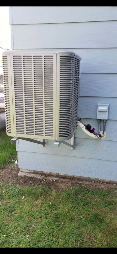An outdoor air conditioning unit mounted on the side of a building by Preferred Heating & Air in Bismarck, ND.