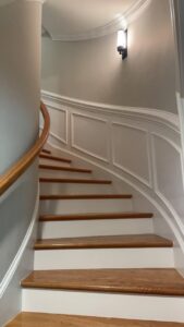 A modern wall sconce light fixture installed above a curved staircase by Geter Electrical Services LLC in Fountain Inn, SC.