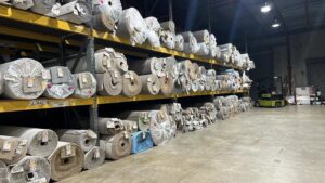 Large warehouse with multiple rolls of carpet stacked on shelves, showing inventory at Gator Carpet and Tile in Jacksonville, FL.