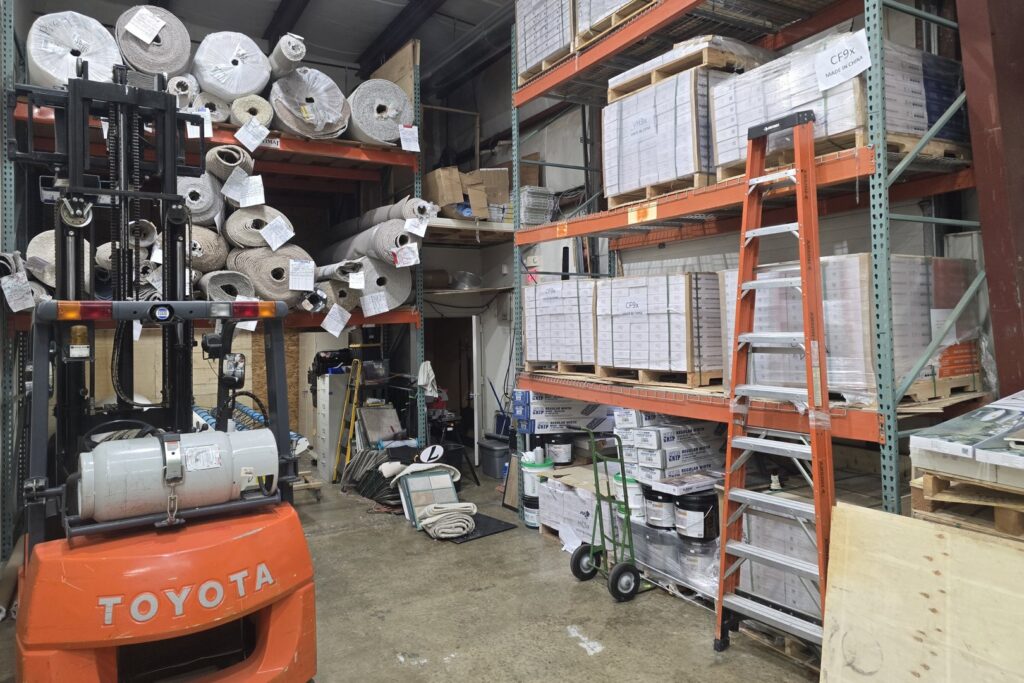 An organized warehouse showing carpet rolls, flooring materials, and a forklift at M&S Flooring Inc. in Ardmore, TN.