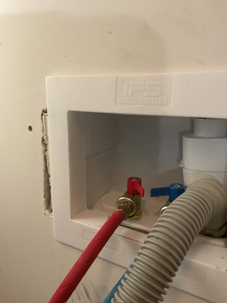 A washing machine plumbing hookup with hot and cold water valves installed by Komfort Air Service Experts in Charlotte, NC.